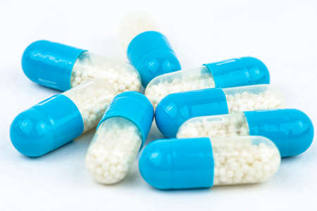 Blue gelatin capsules with white granules inside, isolated on a white background, macro shot.