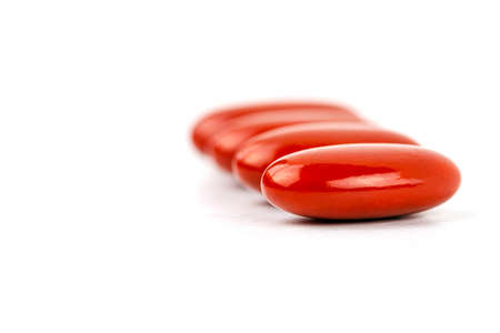A macro shot of four red film-coated tablets arranged in a row, isolated on a white background.