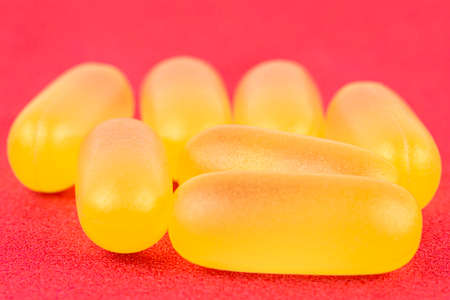 Macro shot of yellow gelatin capsules, isolated on a red background.の写真素材