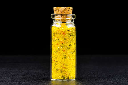 Macro shot of spice from salt and dried vegetables in a small glass bottle closed with a cork, isolated on a black background.の写真素材