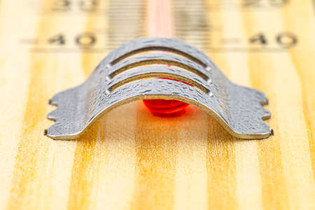 Macro shot of a classic wooden thermometer, visible red alcohol tank and drops of water on a metal...