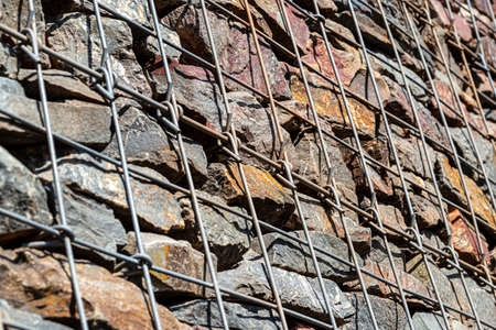 Background made of a stone wall secured with a galvanized metal mesh.