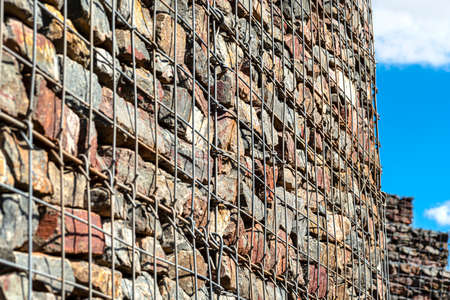 A stone wall standing by the road, made of stones protected by metal, galvanized mesh in the...