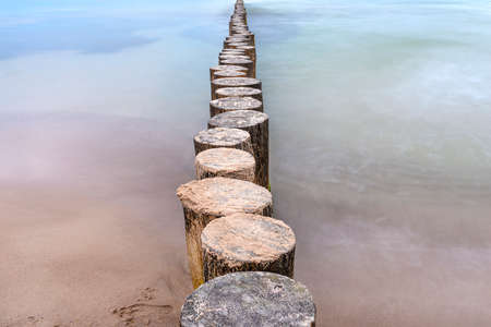Wooden breakwater covered with moss, arranged in a row at sea, long exposure time, blurred sea waves.の写真素材