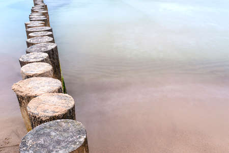 Wooden breakwater covered with moss, arranged in a row at sea, long exposure time, blurred sea waves.の写真素材