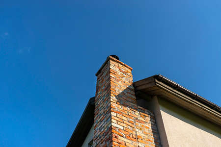 A red ceramic brick chimney standing at the rear of the building, by the facade, with a blue sky in the background.の写真素材