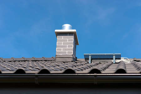 The roof of a single-family house covered with a new ceramic tile in anthracite against the blue sky. Vsible system chimney covered with tiles.の写真素材