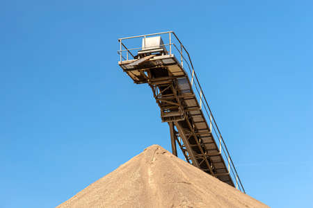 Conveyor belt over heaps of gravel against the blue sky at an industrial cement plant.の写真素材