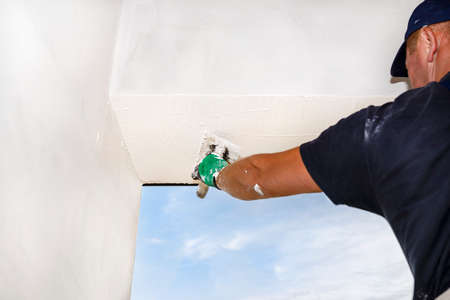 A construction worker applies and blurs a white layer of silicone plaster on the facades of the house.の写真素材