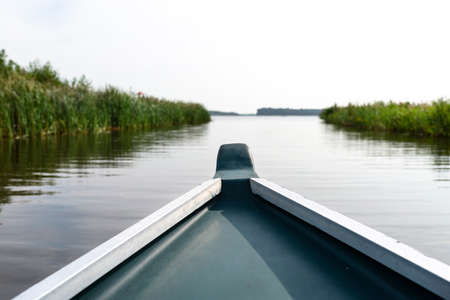 Photo taken from a wooden boat, the prow of the boat visible, in the background a blurry lake and reeds.の写真素材