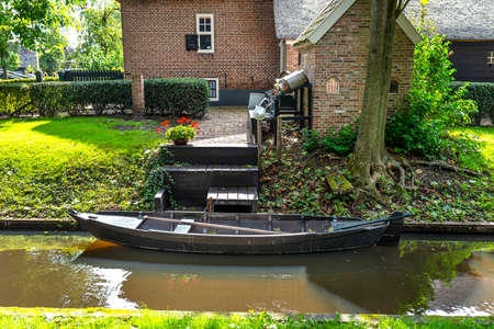 A wooden black boat is moored in a canal by the shore in front of the house, the broadside and rudder are visible.の写真素材