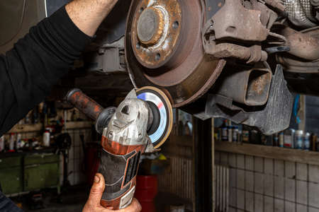 A mechanic grinds, with an angle grinder, the edge of an old rear brake disc in a car, regeneration...