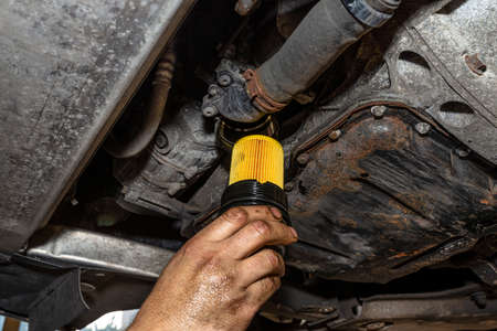 Car mechanic holding a new oil filter for a diesel engine in the background oil pan from the engine.