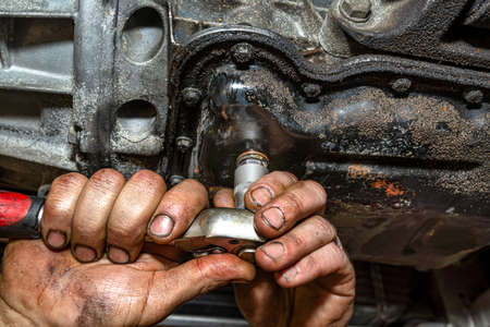The car mechanic bolts a new screw with a copper washer to the oil sump, in a diesel engine.の写真素材