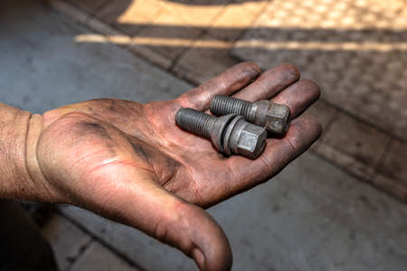 A car mechanic holds in his open, dirty hand metal screws for screwing aluminum and steel rims.の写真素材