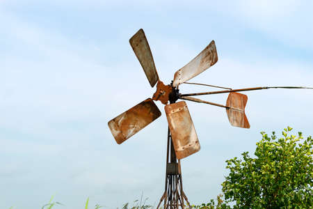 A metal windmill standing on the bank of a canal that runs into a river in the Netherlands.の写真素材