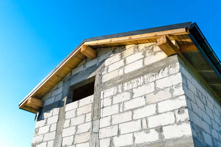 Construction of a small house made of white brick, visible gable roof with boarding and gutter system.の写真素材