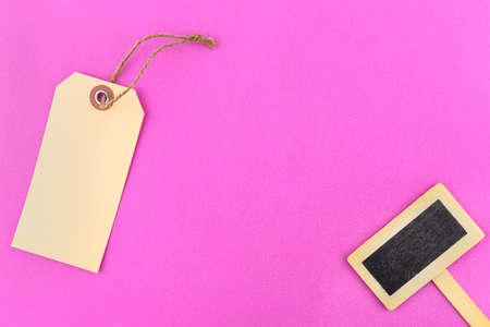 Empty gift tags with a string on the left and a wooden tag on the right, lying on a pink background.