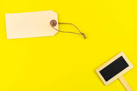 One blank brown gift tags with a string and a wooden tag on the right lying on a yellow background made of sponge.の写真素材