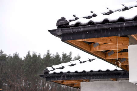 The corner of the roof of a single-family house is covered with snow against the cloudy sky, the...