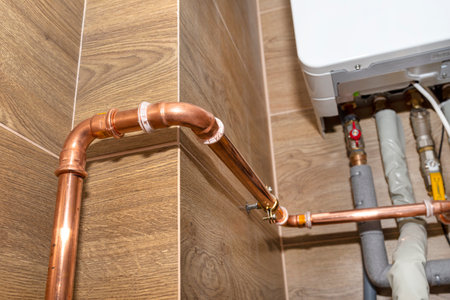 Copper pipes for natural gas installations, attached to a wall in a boiler room lined with ceramic tiles.