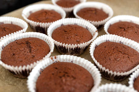 Brown chocolate muffins wrapped in white paper baked in the oven, lying on baking paper.