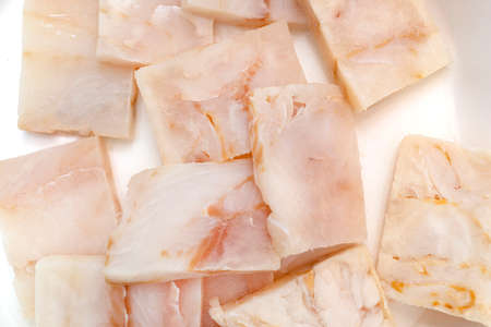 A fresh cod fish fillet cut into squares lying on a white plate, top view.の写真素材
