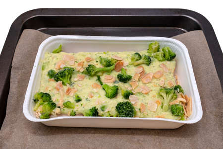 Frozen pollock fillet with broccoli and roasted almonds in a cream sauce lying on baking paper, isolated on a white background.の写真素材