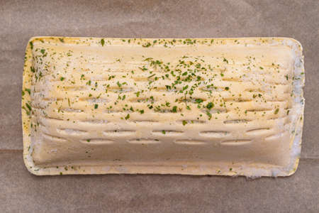 Frozen puff pastry with salmon lying on baking paper, isolated on a brown background top view.の写真素材