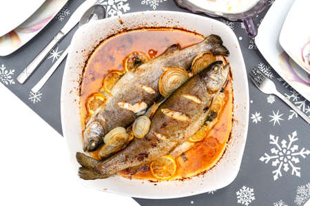 Baked two pieces of trout on a plate with onions and lemon slices dipped in oil on the holiday table, isolatedの写真素材