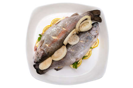 Fresh, raw two trout lying on a plate, stuffed with butter, onion, parsley and lemon slices, isolated on a white backgroundの写真素材