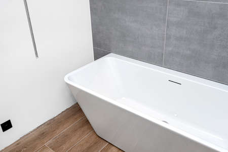 A modern, free-standing wall-mounted bathtub, without a tap, standing in a bathroom lined with...