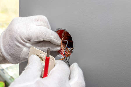 The electrician puts the roller shutter switch up and down in the electrical box in the room by the...