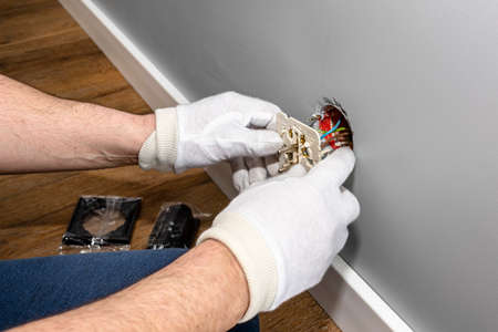 An electrician inserts a double grounded electrical socket into an electrical box in the room wall.