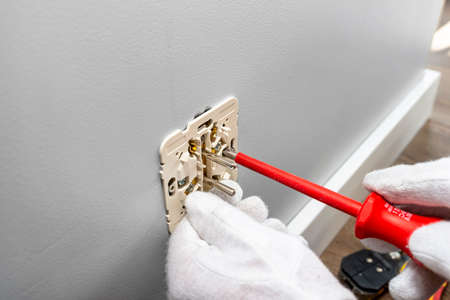 An electrician uses a red screwdriver to screw a double grounded electrical outlet into the...
