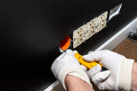 An electrician uses a yellow screwdriver to screw a double grounded electrical socket in a row to...