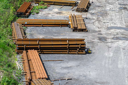 Long and thick, rust-covered steel bars stacked outside on a gravel square, viewed from above.