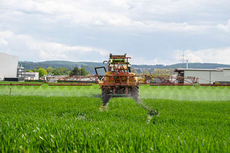 Spraying a crop field with a tractor that has a tank with spray nozzles.の写真素材