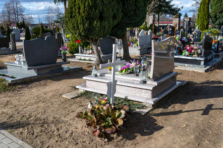 A small cemetery in the countryside with visible tombstones and a small, white wooden cross on a...