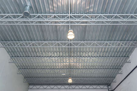 Two light bulbs hanging from the ceiling under a metal lattice in a large industrial warehouse.