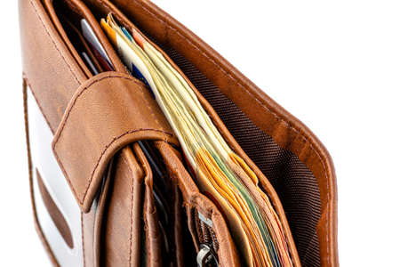 A macro shot of a brown mens leather wallet with a stack of Euro banknotes inside, isolated on a...