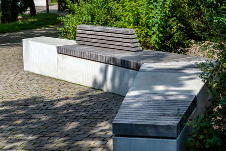 A concrete bench with a wooden seat standing in the park by the sidewalk.の写真素材