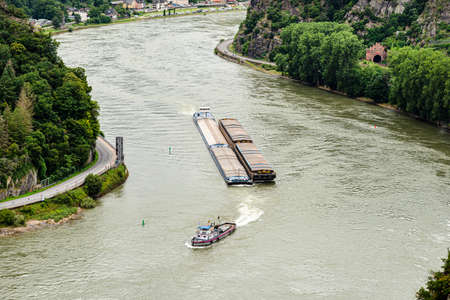 Two barges with a covered deck led by a tugboat on the Rhine river in west Germany, visible road and...