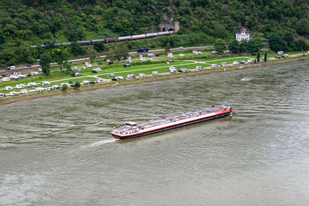 A tanker barge sailing on the river Rhine in western Germany, visible buildings and caravans on the...
