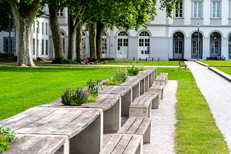Benches and tables with flowers arranged in a row in the park, in the background a large building with arched windows.の写真素材