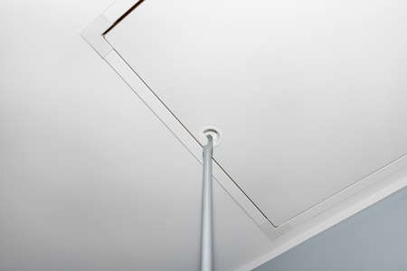 Folding metal stairs to the attic in the ceiling, closed hatch with a tube for opening, modern look.の写真素材