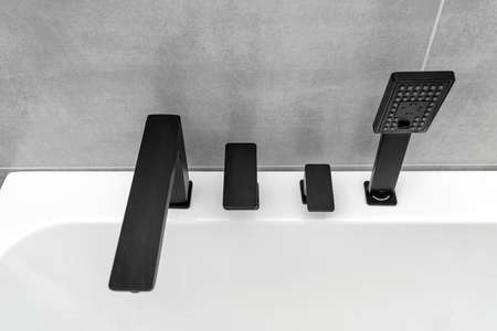 A modern, free standing wall mounted bathtub with a black matt tap, standing in a bathroom lined...