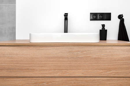 A modern washbasin in the bathroom in a wall mounted cupboard with a matte black faucet, a wall lined with gray ceramic tiles.の写真素材