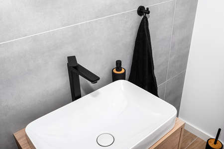 A modern washbasin in the toilet in a wall mounted cupboard with a matte black faucet, a wall lined with gray ceramic tiles.の写真素材