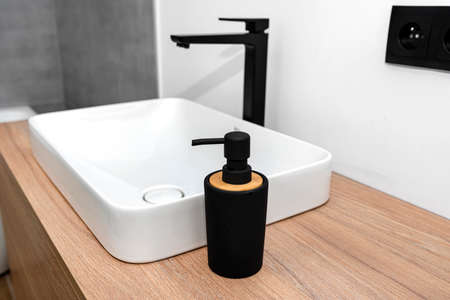 A modern washbasin in the bathroom in a wall mounted cupboard with a matte black faucet, a wall lined with gray ceramic tiles.の写真素材